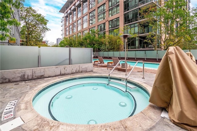 pool with fence, a hot tub, and a patio area