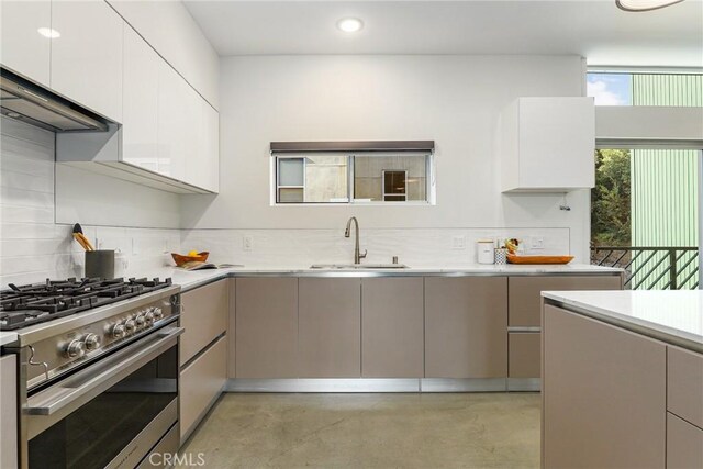 kitchen with a sink, decorative backsplash, stainless steel gas stove, light countertops, and finished concrete flooring