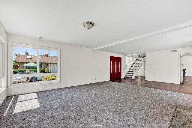 unfurnished living room featuring baseboards, dark colored carpet, visible vents, and stairs