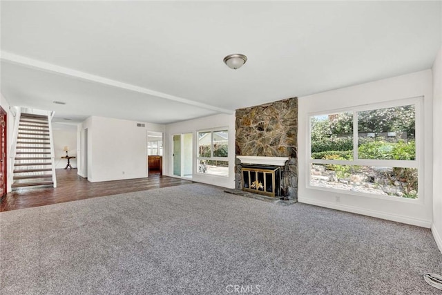 living room with a fireplace, stairs, dark carpet, and plenty of natural light