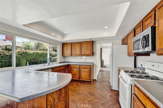 kitchen with stainless steel microwave, brown cabinetry, a raised ceiling, white gas range, and a peninsula