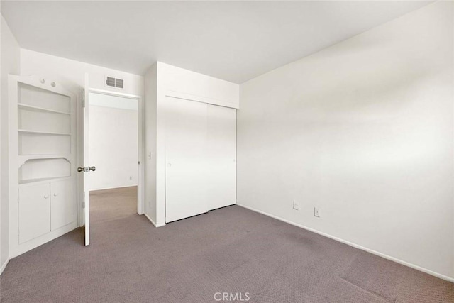 unfurnished bedroom featuring baseboards, visible vents, dark carpet, and a closet