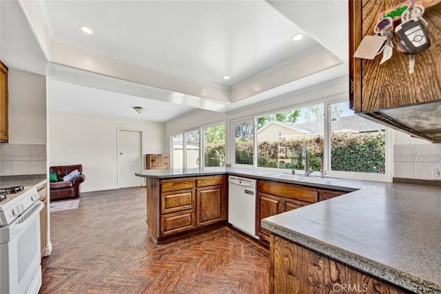 kitchen featuring white appliances, brown cabinetry, ornamental molding, a sink, and a raised ceiling