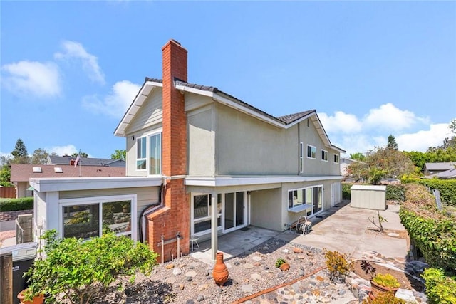 rear view of property featuring a patio, a chimney, and stucco siding