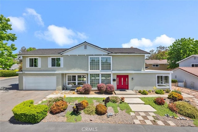 traditional-style home with driveway, an attached garage, a tiled roof, and stucco siding