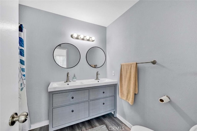 full bathroom featuring double vanity, a sink, wood finished floors, and baseboards