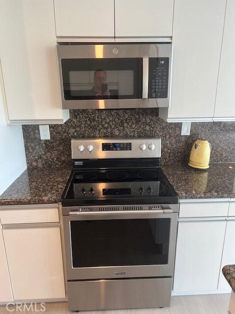 32679 Seagate Dr Unit 308-H, Rancho Palos Verdes, CA 90275 - kitchen with dark stone counters, appliances with stainless steel finishes, white cabinets, and backsplash