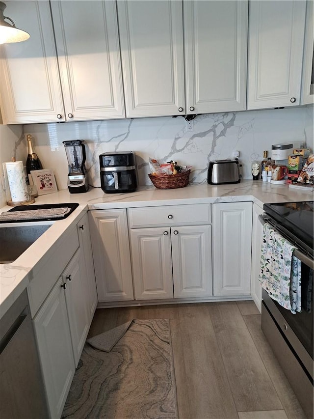kitchen with decorative backsplash, light stone countertops, white cabinetry, light wood finished floors, and stainless steel appliances