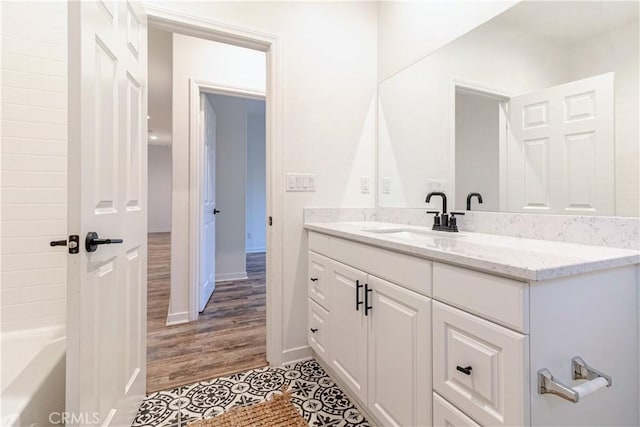 full bathroom with wood finished floors, baseboards, a washtub, and vanity