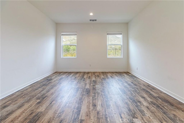 empty room with a wealth of natural light, visible vents, wood finished floors, and baseboards