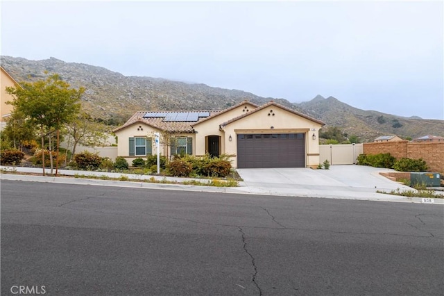 mediterranean / spanish-style home with a mountain view, fence, solar panels, an attached garage, and stucco siding