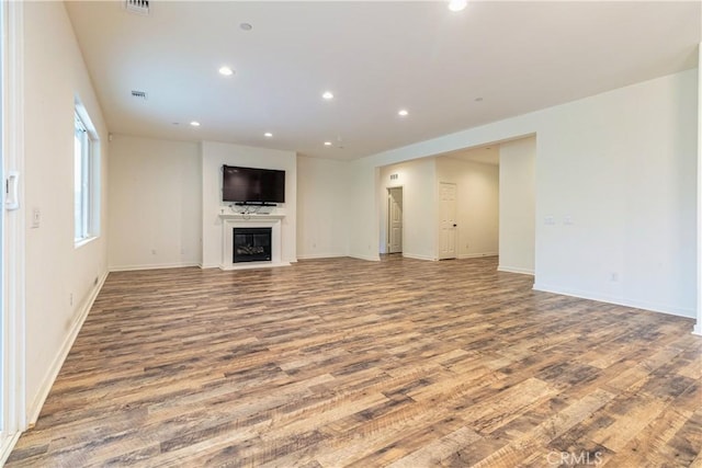 unfurnished living room featuring recessed lighting, baseboards, a glass covered fireplace, visible vents, and wood finished floors