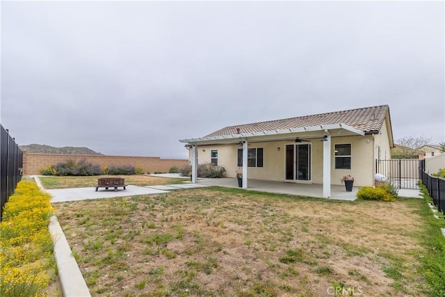 rear view of house featuring an outdoor fire pit, stucco siding, a fenced backyard, ceiling fan, and a patio area