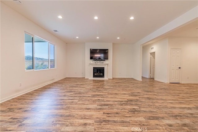 unfurnished living room featuring recessed lighting, a glass covered fireplace, and wood finished floors