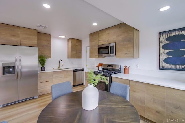 kitchen with stainless steel appliances, a sink, modern cabinets, recessed lighting, and light wood-style floors