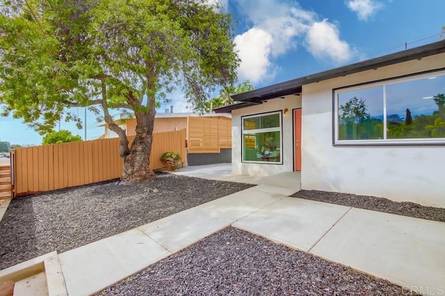 view of side of property featuring fence, stucco siding, and a patio