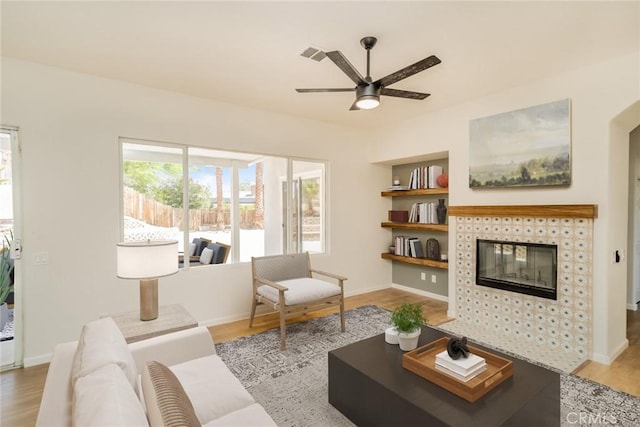 living area featuring a tiled fireplace, visible vents, wood finished floors, and a ceiling fan