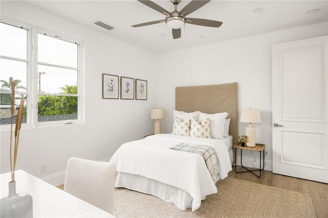 bedroom with baseboards, a ceiling fan, wood finished floors, and visible vents