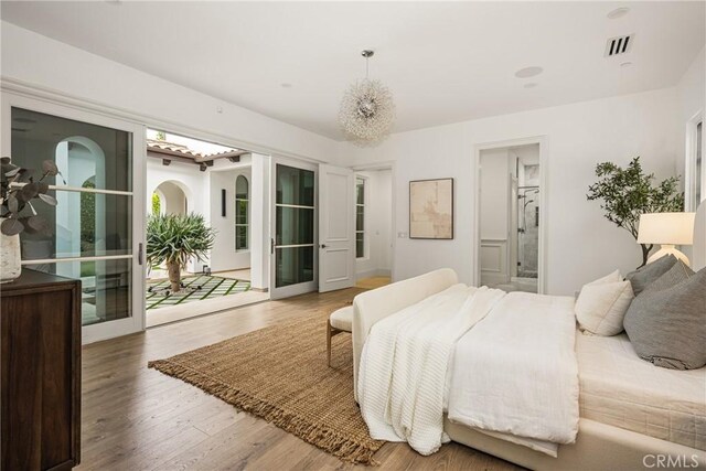 bedroom with visible vents, ensuite bathroom, wood finished floors, and access to exterior