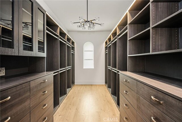 walk in closet featuring light wood-type flooring and a notable chandelier