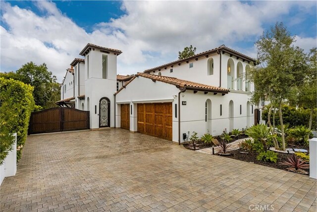 mediterranean / spanish-style house with a tile roof, a gate, a garage, decorative driveway, and stucco siding