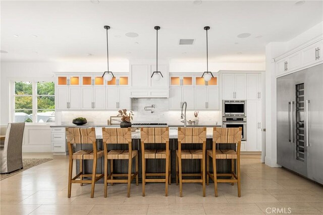 kitchen with a large island with sink, stainless steel built in fridge, backsplash, visible vents, and glass insert cabinets