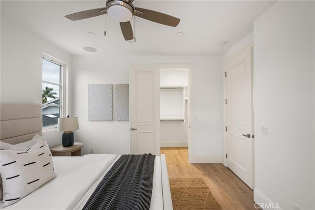 bedroom with baseboards, ceiling fan, a walk in closet, and light wood finished floors