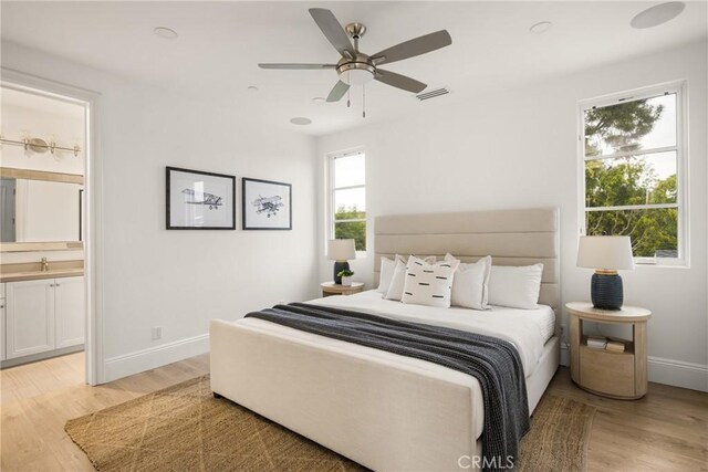 bedroom with visible vents, baseboards, a sink, light wood finished floors, and ensuite bath