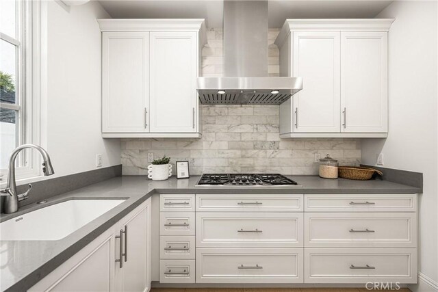kitchen with wall chimney range hood, white cabinets, stainless steel gas cooktop, and a sink