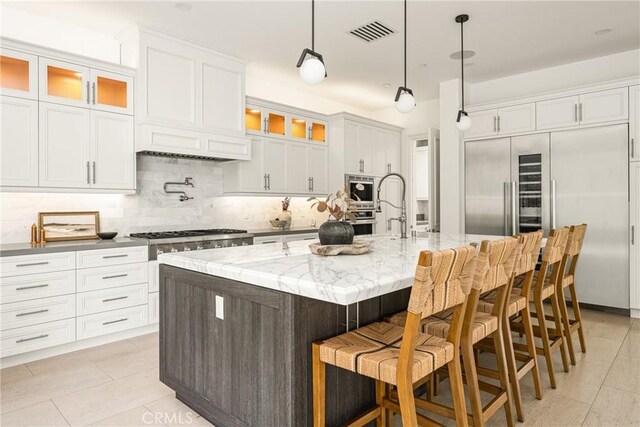 kitchen with backsplash, visible vents, a center island with sink, a sink, and built in appliances