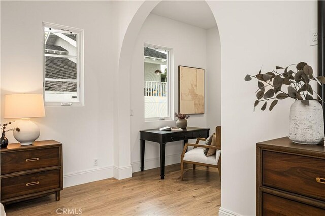 interior space featuring light wood-style floors, arched walkways, and baseboards