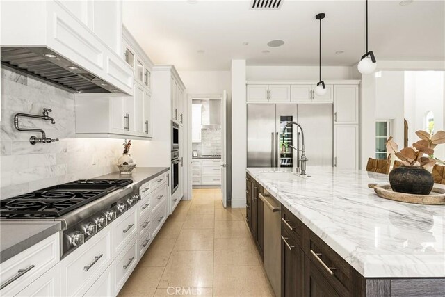 kitchen featuring decorative backsplash, a kitchen island with sink, appliances with stainless steel finishes, white cabinets, and custom exhaust hood
