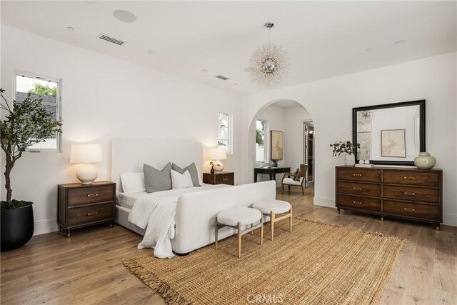 bedroom with visible vents, arched walkways, baseboards, and wood finished floors
