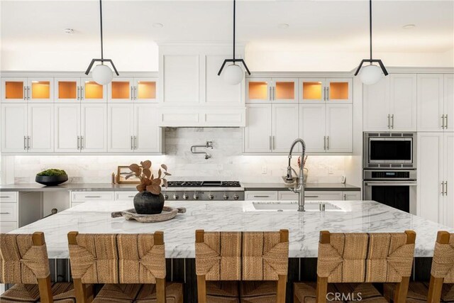 kitchen featuring decorative backsplash, appliances with stainless steel finishes, a center island with sink, a sink, and white cabinetry