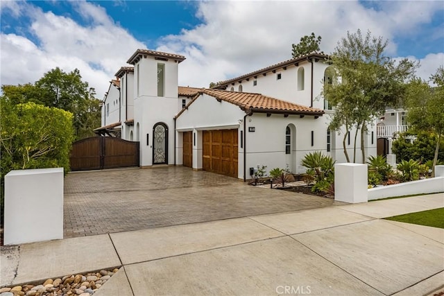 view of front facade featuring stucco siding, a gate, a tiled roof, an attached garage, and driveway