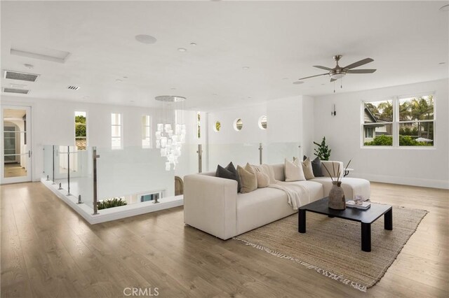 living room with a wealth of natural light, ceiling fan with notable chandelier, and wood finished floors