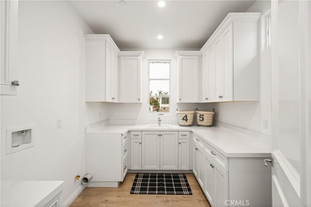 laundry room with cabinet space, a sink, light wood finished floors, hookup for a washing machine, and recessed lighting