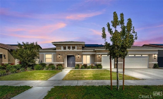 prairie-style home with a garage, a lawn, stone siding, concrete driveway, and solar panels