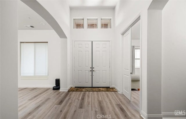 entrance foyer featuring arched walkways, baseboards, light wood-style flooring, and plenty of natural light