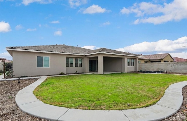 rear view of house with stucco siding, fence, a yard, and a patio
