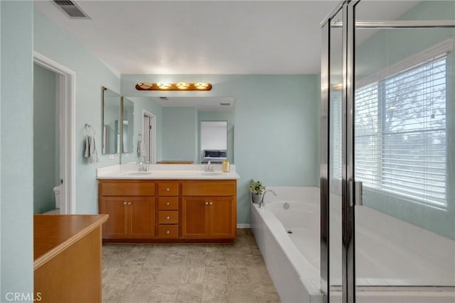 bathroom featuring double vanity, visible vents, a bath, and a sink