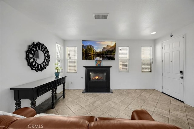 living room featuring visible vents, light tile patterned flooring, and a glass covered fireplace