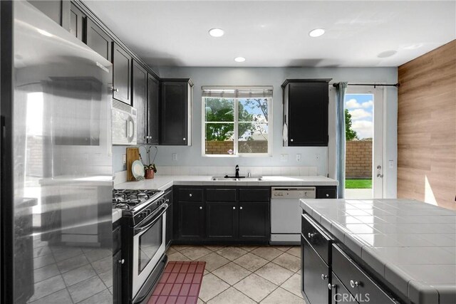 kitchen featuring recessed lighting, light tile patterned floors, stainless steel appliances, tile counters, and a sink