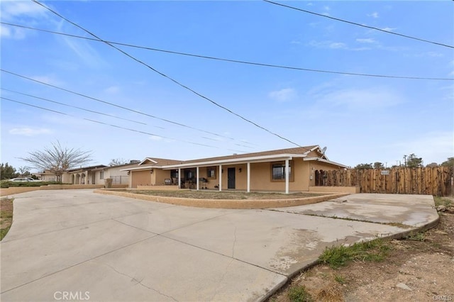 ranch-style house with driveway, fence, covered porch, and stucco siding