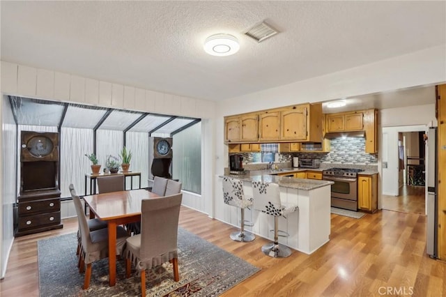 4447 Walnut Ave, Chino, CA 91710 - kitchen with tasteful backsplash, a peninsula, under cabinet range hood, gas stove, and a textured ceiling