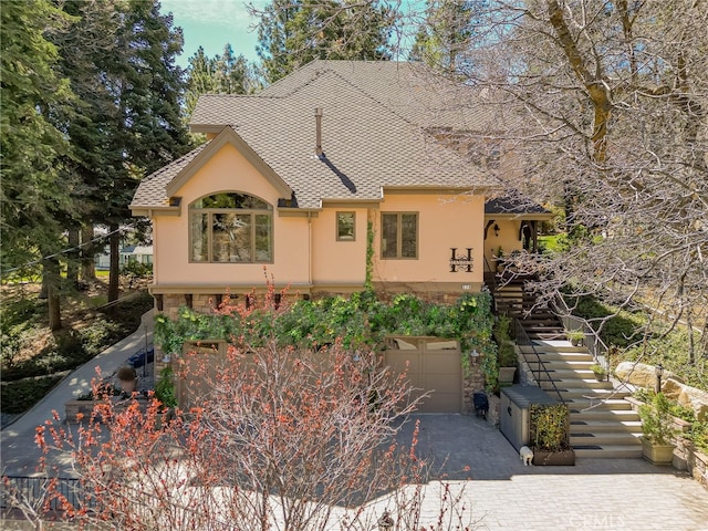 view of front facade featuring stairs, aphalt driveway, stone siding, an attached garage, and stucco siding