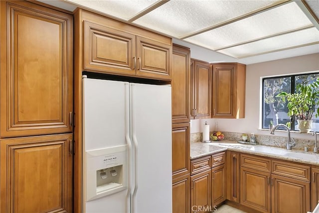 21650 Burbank Blvd Unit 111, Woodland Hills, CA 91367 - kitchen featuring white refrigerator with ice dispenser, a sink, light stone counters, and brown cabinetry