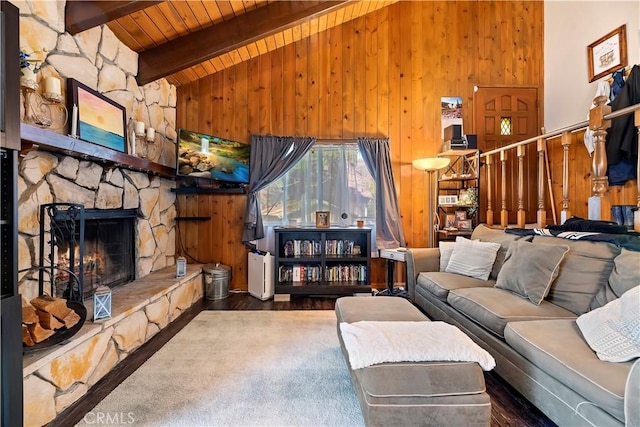 living area featuring lofted ceiling with beams, wooden ceiling, wooden walls, wood finished floors, and a stone fireplace