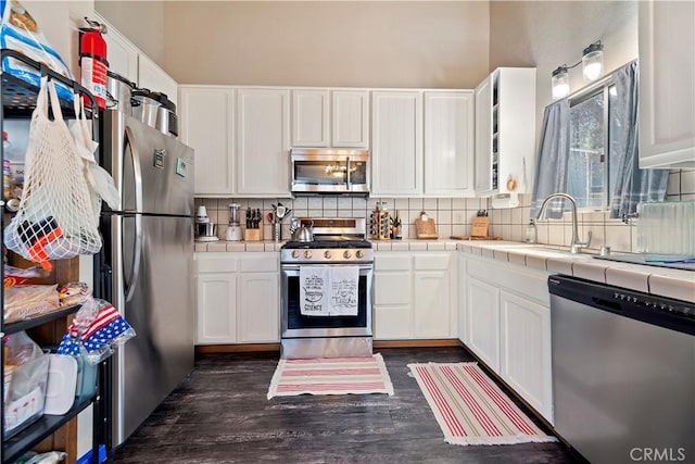 kitchen with white cabinetry, decorative backsplash, tile counters, stainless steel appliances, and dark wood-type flooring