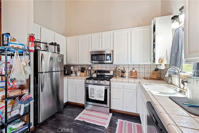 kitchen featuring a sink, tile counters, appliances with stainless steel finishes, and white cabinetry